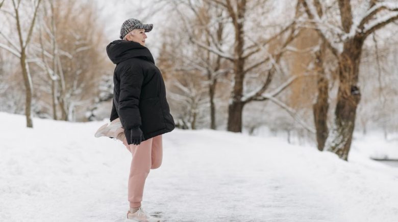 An elderly woman warms up for exercise in a snowy park.